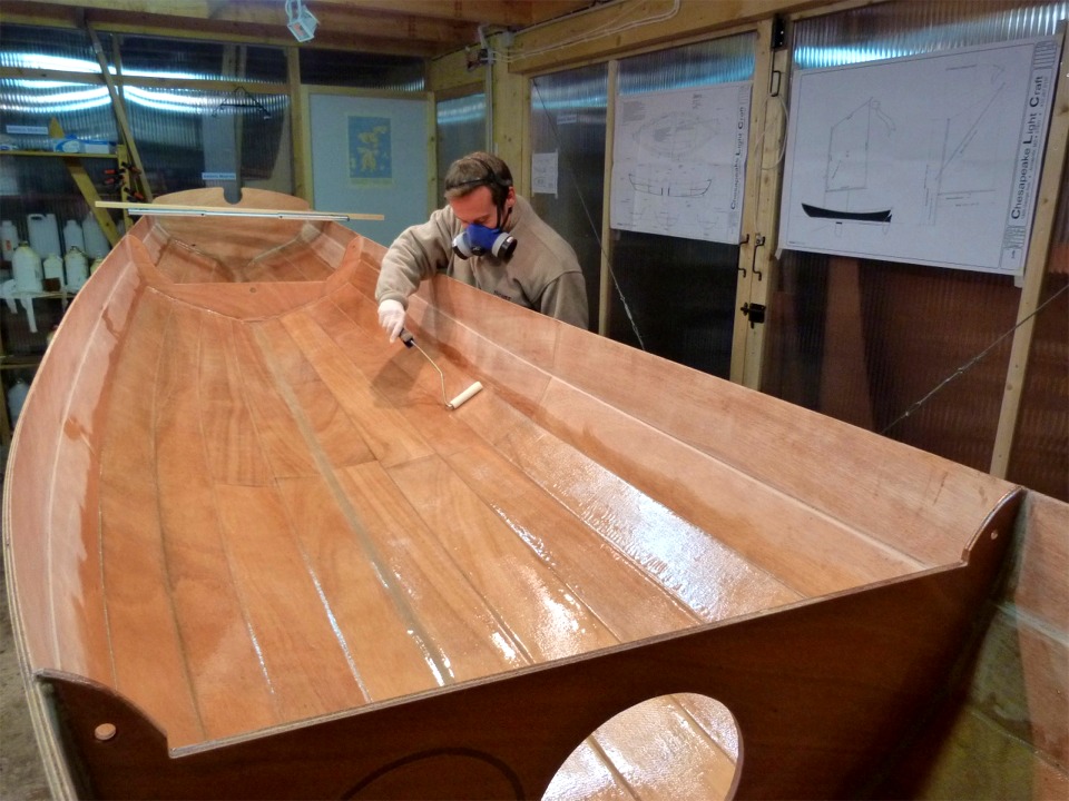 Quatre heures après avoir fini de saturer le tissu de verre, Arnaud passe une nouvelle couche d'époxy au rouleau sur toute la surface stratifiée afin de "remplir la trame" du tissu. En effet, lors de la stratification, on ne met pas trop d'époxy car le tissu doit être saturé mais sa trame doit être clairement apparente. Si on mettait trop de résine, le tissu risquerait de "flotter" et le composite CP-fibre de verre-époxy ne serait pas homogène. On laisse donc durcir partiellement la stratification "maigre", puis on ajoute une nouvelle couche de résine par dessus, et cette nouvelle couche va fusionner avec la première, déjà assez durcie pour que le tissu reste bien collé au CP. Le but de cette seconde couche est esthétique : il s'agit de réduire le relief causé par la trame afin que le tissu devienne totalement invisible sous le vernis ou la peinture. 