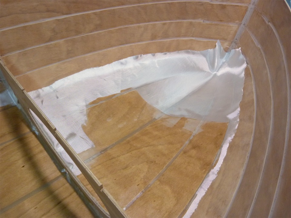 Je verse la résine époxy sur le tissu de verre, puis je l'étale et la fais pénétrer dans la trame du tissu à l'aide de la "squeegee". J'ai enlevé la bande de renfort de l'étrave pour saturer la pièce principale, je m'en occuperai juste après. 