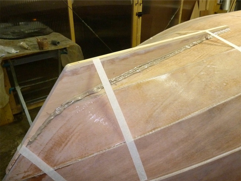 Voici de nouvelles images du Skerry "Christophine" dont la construction continue à l'atelier. Voici le collage de l'aileron : j'ai d'abord enduit la tranche de l'aileron d'une bonne couche d'époxy chargée, je l'ai posé sur les tracés de positionnement que j'avais fait sur la sole, j'ai collé trois bandes d'adhésif pour le maintenir en place. J'ai ensuite vérifié son orthogonalité par rapport à la sole (on est bien guidé par la partie qui remonte sur l'étambot, mais il faut tout de même s'en assurer), puis j'ajoute de l'époxy chargée de part et d'autre de l'aileron afin de faire de gros joints-congés de part et d'autre. 