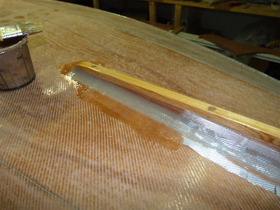 J'ai commencé par appliquer une couche d'époxy sur le joint, j'ai mis la bande de fibre en place, et je la sature au pinceau. On voit sur la droite de l'image que le tissu est déja partiellement mouillé par l'époxy appliquée sur le joint. 