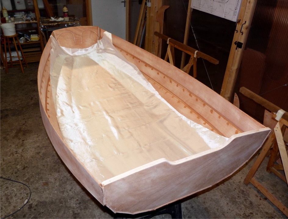 Je drape le tissu de verre sur la surface intérieure. Ce tissu d'un mètre de large couvrira la sole et les deux bordés 1. Un second tissu de verre sera ultérieurement stratifié sur la même zone à l'extérieur de la coque. Les bordés 2, 3 et 4 seront seulement couverts de deux couches d'époxy qui durciront la surface du bois et la rendront étanche. 