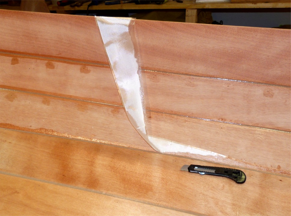 Je coupe la fibre de verre avec un cutter (lame neuve, car la fibre est un peu délicate à couper) en m'appuyant sur le joint d'époxy entre les bordés 1 et 2. En effet, pas question de couper sur le contreplaqué car la pointe de la lame ferait une marque permanente. 
