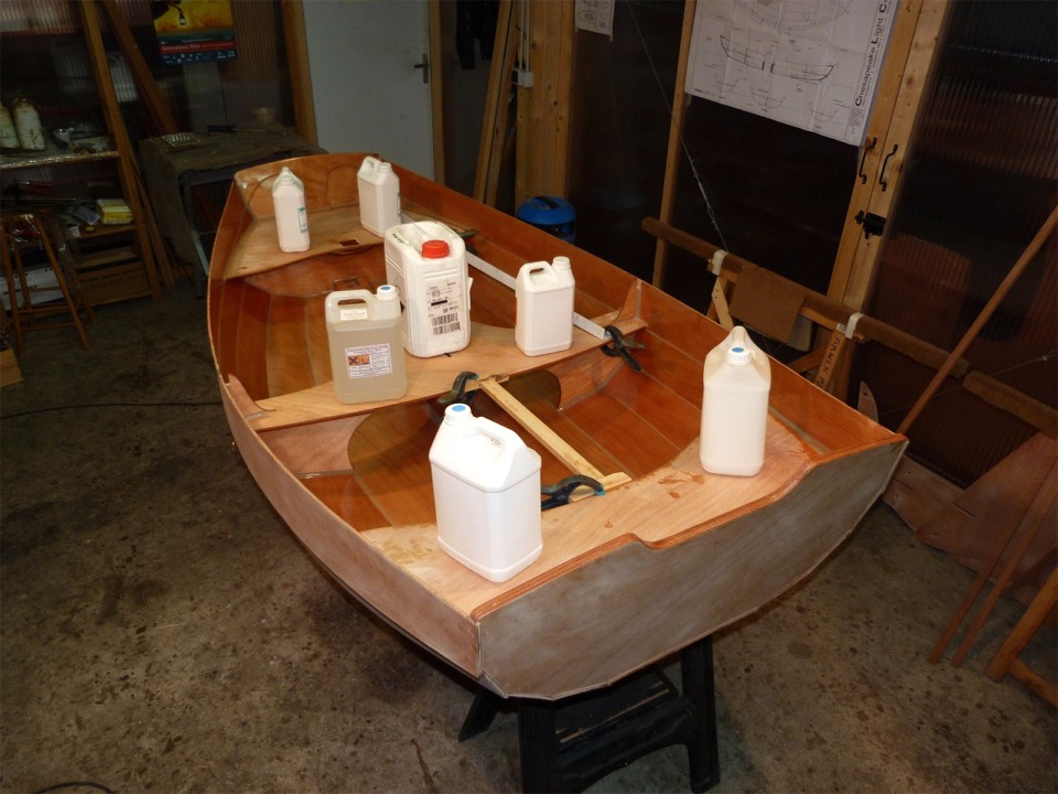 Après avoir collé le pied de mât, j'ai passé une nouvelle couche d'époxy sur toute la surface intérieure de la Prame d'Eastport, sur le dessous des sièges, et j'ai collé ceux-ci en place. Les bidons exercent un peu de pression sur les collages. Les tasseaux fixés avec des pinces bloquent les sièges avant et arrière qui ont tendance à glisser vers le centre du bateau du fait de leur angle. Je ferai les joints-congés sous les sièges ultérieurement, un fois la coque retournée. 
