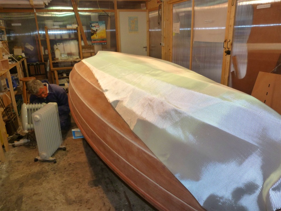 Après un dépoussiérage complet, nous rentrons le bateau et drapons le tissu de 300 g/m2. Pierre est occupé à glisser le petit radiateur sous la coque afin de la garder au chaud pendant la nuit prochaine. 