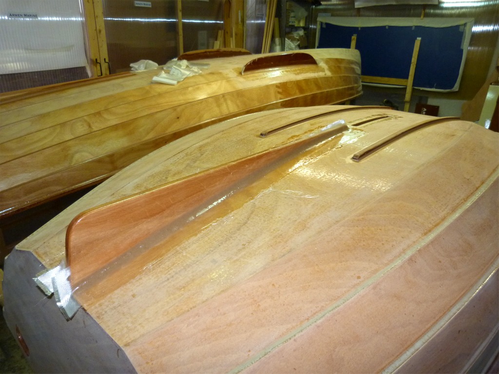 J'ai totalement saturé d'époxy les bandes de fibre de verre sur les joints-congés de part et d'autre de l'aileron de la Prame d'Eastport, et posé celles qui renforcent les arêtes de l'ouverture du puits de dérive. On aperçoit à l'arrière-plan sur la Yole de Chester de Pierre les bandes de fibre de verre qui vont me servir à renforcer la fixation de son aileron.