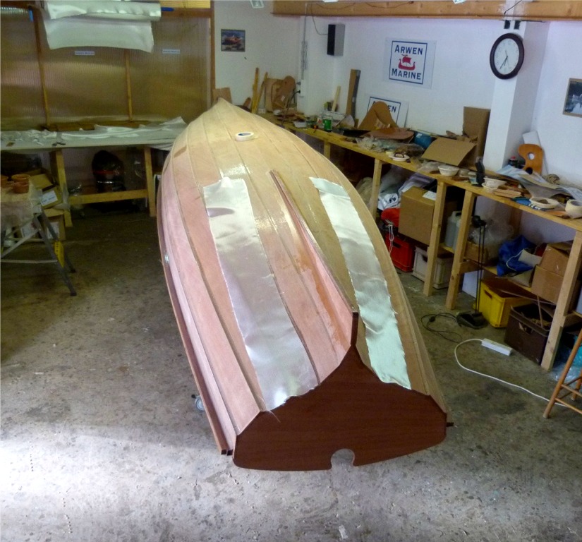 Sous cet angle, la Yole de Chester a l'air d'être en lévitation, car on ne voit pratiquement pas le chariot et les tréteaux. Je m'apprête à stratifier les bandes de tissu de verre sur les cotés de l'aileron afin de renforcer son collage. 