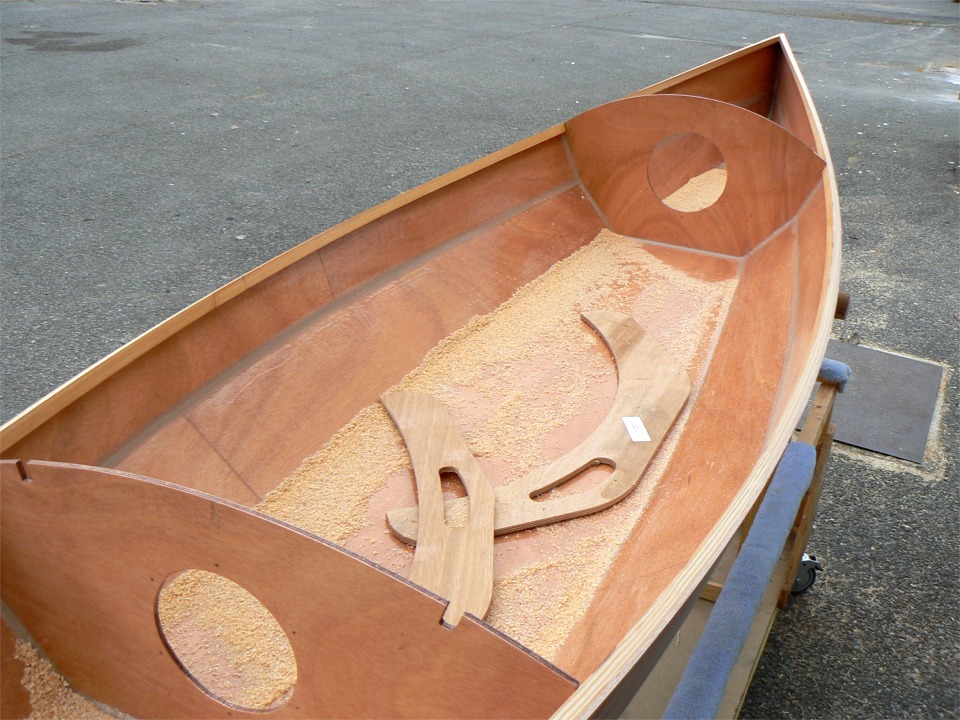 Après durcissement, je remets la coque à l'endroit et je la sors dehors pour passer un coup de rabot sur les serres bauquières afin de leur donner un angle correspondant au bouge du pont. Celui-ci est beaucoup plus marqué à l'avant qu'à l'arrière, comme les observateurs avisés l'auront noté. Les deux pièces en arc de cercle posés dans la sciure sont les "guides de rabotage" fournis avec le kit, qui permettent de vérifier l'angle donné aux bauquières. 