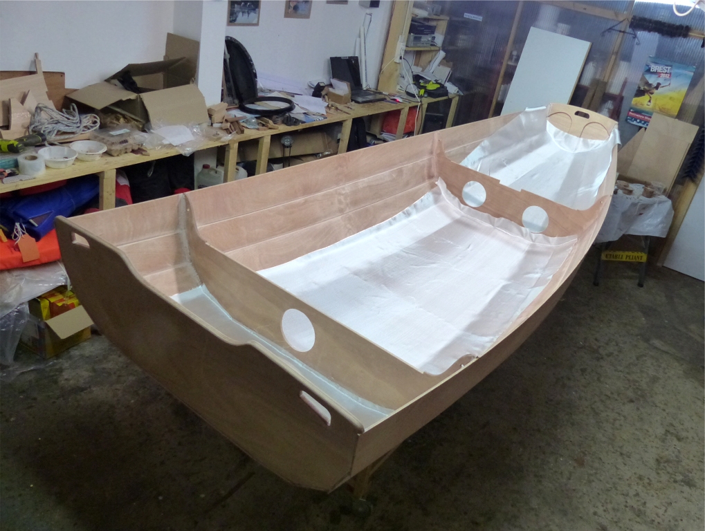 Je drape trois pièces de tissu de verre sur la surface intérieure basse de la coque. En effet, la stratification est volontairement limitée à la sole et aux bordés 1, car cela suffit à rigidifier la coque et à protéger la surface intérieure dans la zone où elle sera piétinée. Le surpoids d'une stratification intégrale serait peu justifié. De plus, les tissus les plus courants sont disponibles en largeur d'un mètre, ce qui convient à la zone visée. Il n'y a qu'à l'avant que je couvre aussi les bordés 2 afin de rigidifier un peu plus la proue. 