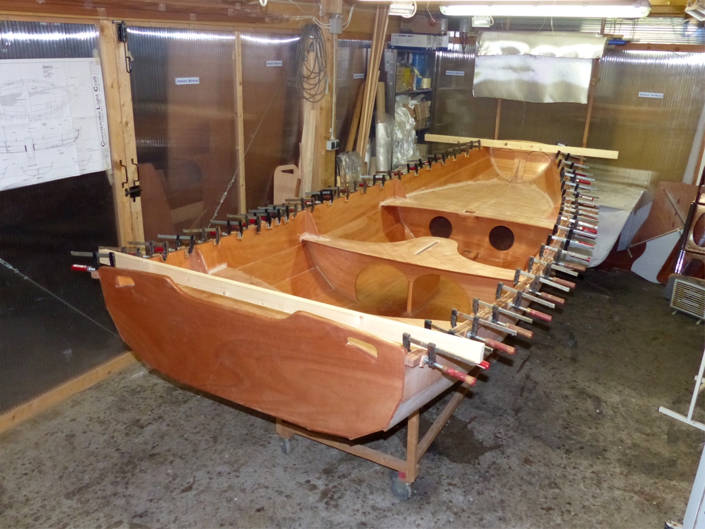 Après avoir avoir poncé la surface de tous les joints-congés réalisés la veille, je rentre le PassageMaker Dinghy dans la partie chauffée de l'atelier et je colle les listons. Les tasseaux posés en travers de la coque à l'avant et à l'arrière me servent à vérifier visuellement que le bateau n'est plus vrillé. 