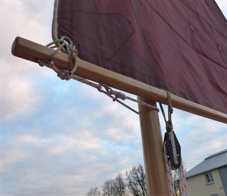 Même vue, coté voile. On voit ici la poulie haute du palan d'amure à 4 brins. Son capelage est fait d'une simple boucle en cordage passée en double et nouée par un noeud de pêcheur. Un pontet inox sur le dessus de la bôme fixe le capelage en longitudinal. Notez ma confiance absolue dans les collages à l'époxy : le scarf est placé à l'endroit du capelage, qui est celui de plus forte contrainte sur la bôme ! 